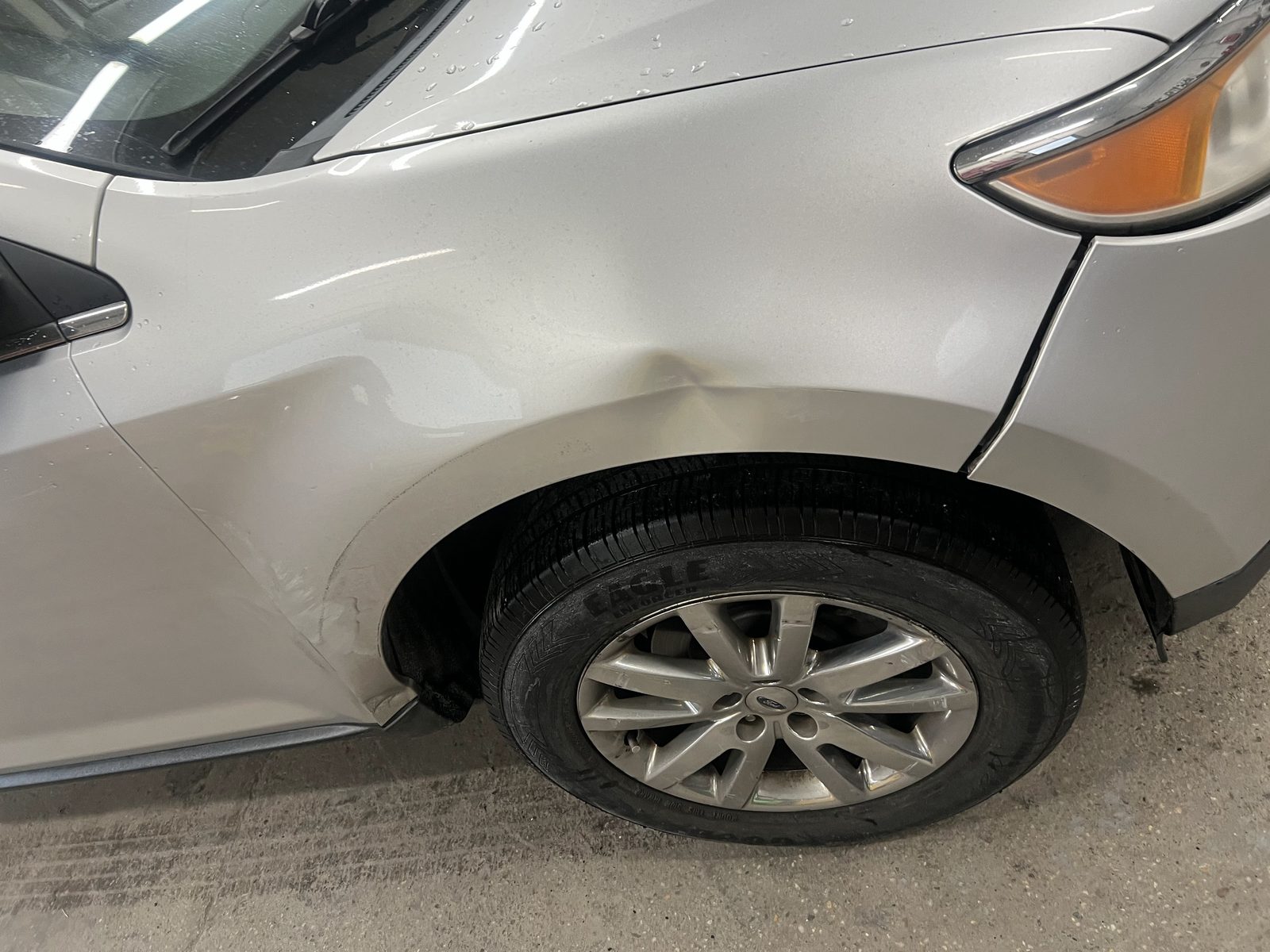 Silver Ford SUV with a dented front fender inside the Grand National Collision shop