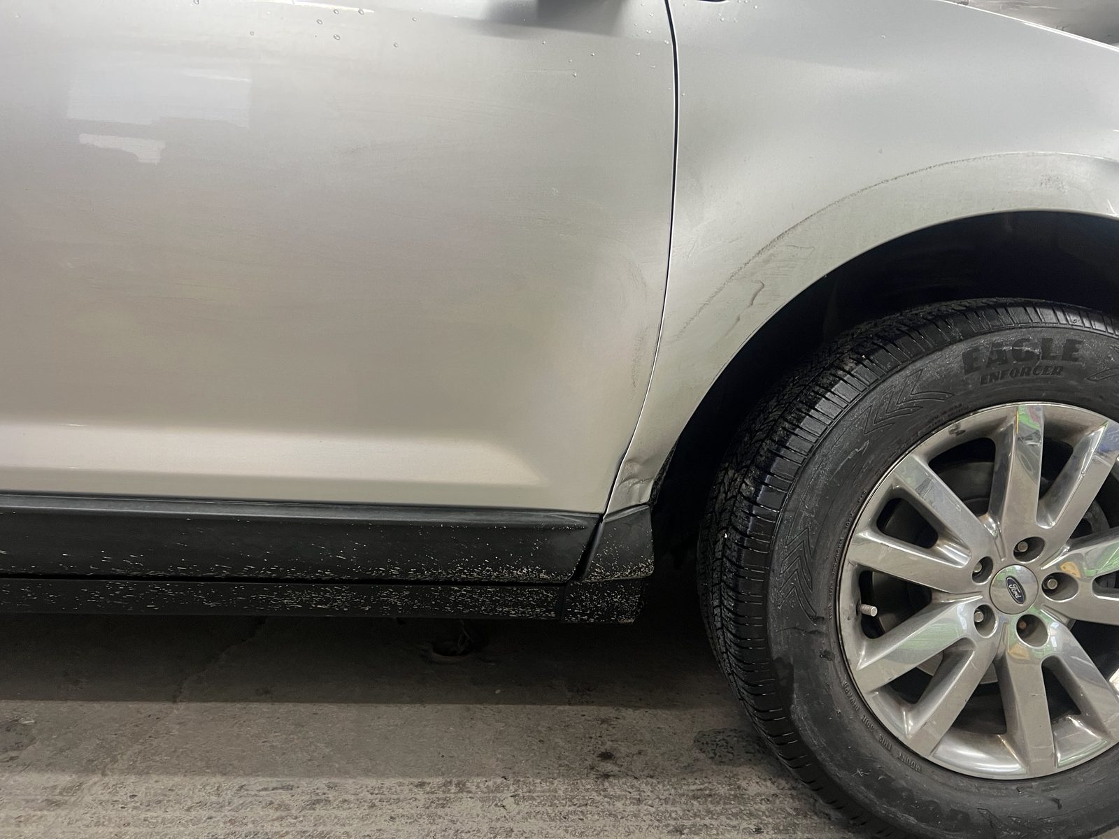 Silver Ford SUV with a small dent above the rear wheel and road debris along the rocker panel