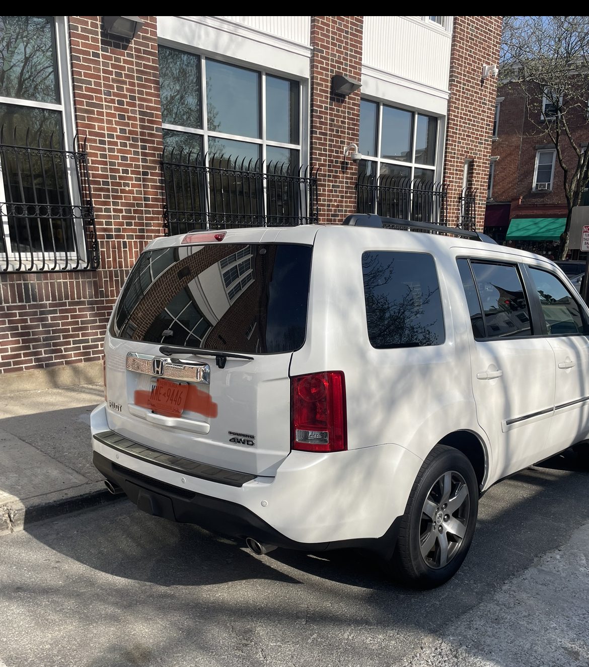 White Honda Pilot parked on a street beside a brick building