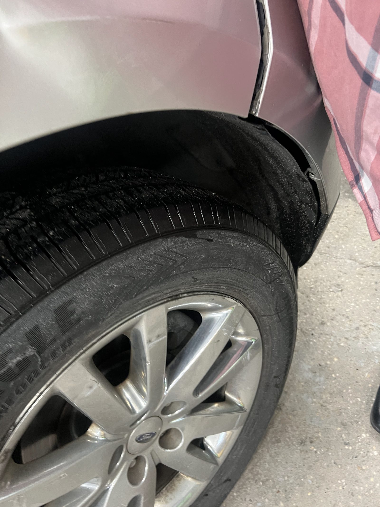 Close-up of collision damage along the wheel arch and lower fender of a silver car
